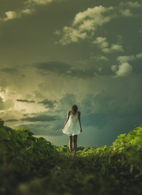 woman wearing white dress standing on hill with green grass under white cloudy sky