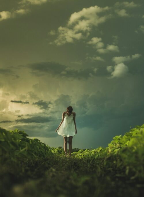 woman wearing white dress standing on hill with green grass under white cloudy sky