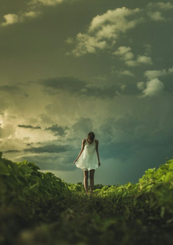 woman wearing white dress standing on hill with green grass under white cloudy sky