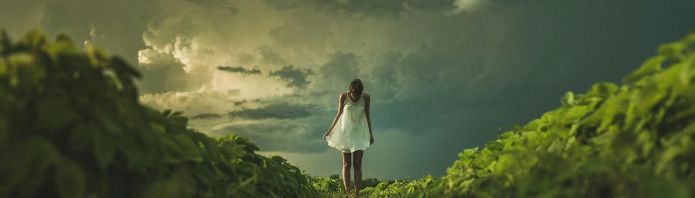 woman wearing white dress standing on hill with green grass under white cloudy sky