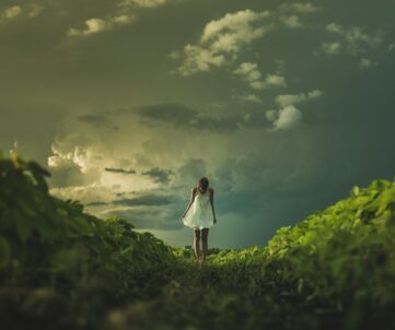 woman wearing white dress standing on hill with green grass under white cloudy sky