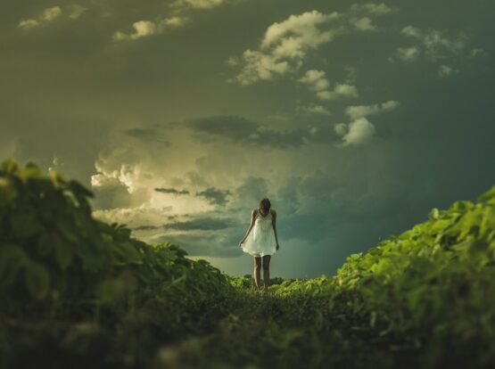 woman wearing white dress standing on hill with green grass under white cloudy sky