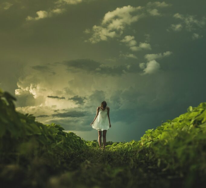 woman wearing white dress standing on hill with green grass under white cloudy sky