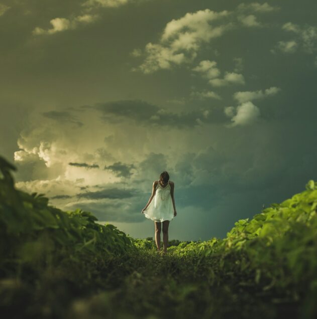 woman wearing white dress standing on hill with green grass under white cloudy sky